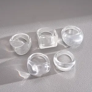 High-quality macro view of five-piece set transparent resin geometric rings on grey leather.
