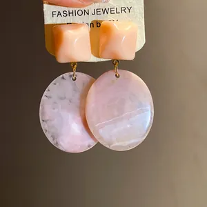 Close-up of vintage resin earrings with square studs and marble-patterned oval pendants.