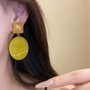Macro detail of resin drop earrings featuring square and oval geometric Maillard design