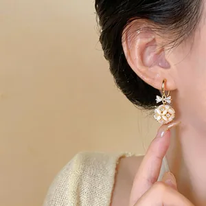 Elegant 14k gold-plated cat-eye stone floral bow drop earrings shown on a model's ear