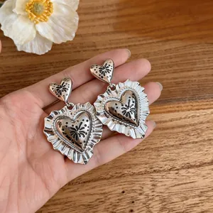Vintage silver heart drop earrings with ruffled lace edges held in hand for scale