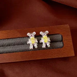 Close-up of silver bear stud earrings with yellow and green zircons on wooden tray.