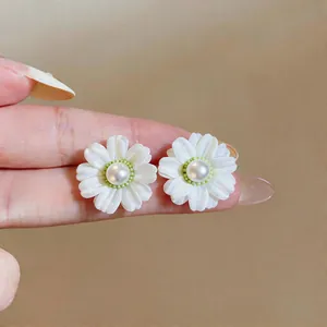 Detailed view of white fabric daisy stud earrings with central pearl accents.
