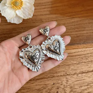 Detailed close-up of vintage silver heart-shaped earrings with ruffled edges on hand