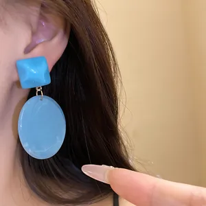 Detailed close-up showing the blue resin square and oval drop earrings worn on ear