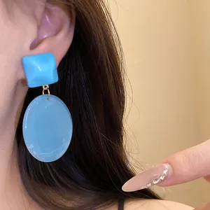 Detailed close-up shot of blue resin square and oval pendant earrings worn on ear