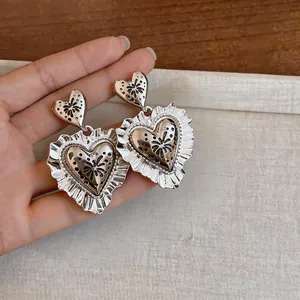 Detailed view of silver heart earrings with intricate flower engravings and ruffled edges.