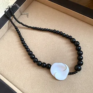 Primo piano di una collana di perle nere con un ciondolo a fiore in smalto bianco in un vassoio