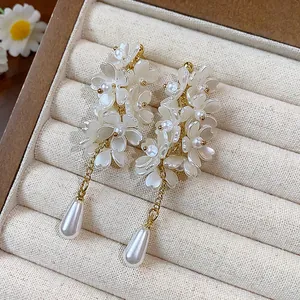 Macro detail of white resin flower earrings with gold chain and teardrop pearls