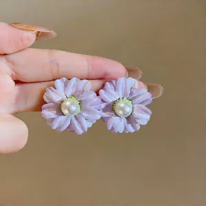Detailed shot of purple fabric flower stud earrings with pearl centers held in hand