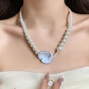 Elegante collana di perle con ciondolo a fiore in smalto bianco, dettaglio indossato.
