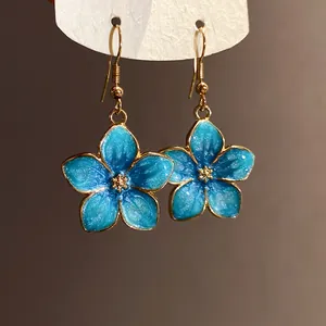 Detailed macro view of elegant shimmering blue enamel flower earrings with golden hooks.