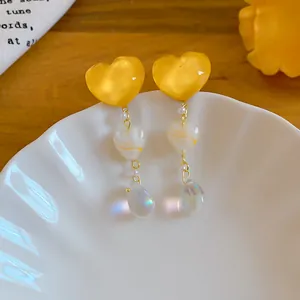 Close-up of vintage yellow heart earrings with iridescent drop beads on a plate.