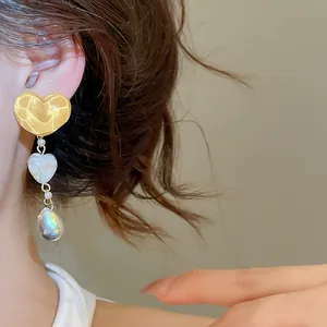 Detail view of vintage irregular yellow heart tassel earrings with iridescent drop on model