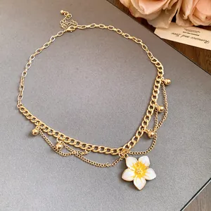 Detail view of a vintage gold chain necklace featuring a white plumeria flower pendant.