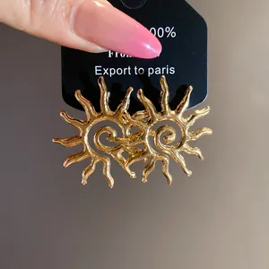 Detail view of gold sun-shaped hollow metal stud earrings with textured finish