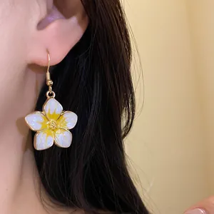Close-up of yellow and white plumeria flower earring with a sparkly finish worn on ear.
