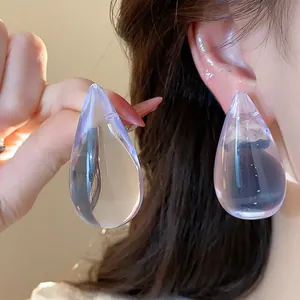 Primer plano de pendientes de gota de resina morada con agujas de plata elegantes.