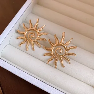 Close-up detail of golden sun-shaped hollow metal stud earrings in a box
