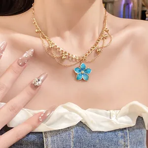 Detail of a vintage gold layered necklace with a vibrant blue enamel flower pendant on model.