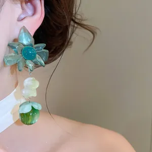Close-up view of a green translucent floral dangle earring featuring a cute animal bead detail