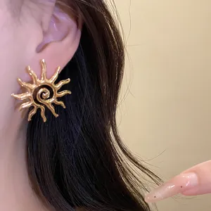 Macro detail of an elegant gold sun hollow stud earring with spiral design worn on the ear