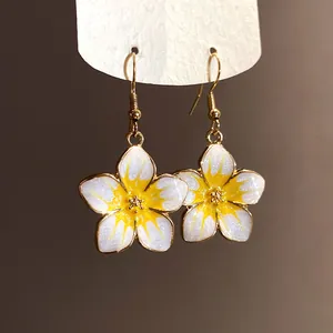 Detailed view of white and yellow enamel flower drop earrings with a glittery finish.