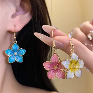 Close-up of colorful enamel flower earrings featuring gold hooks and glitter finish