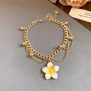 Detail of gold layered anklet featuring a white and yellow enamel flower pendant