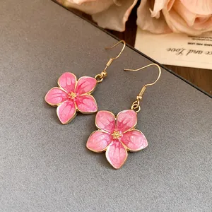 Detail view of pink enamel flower earrings with gold hooks on textured background.