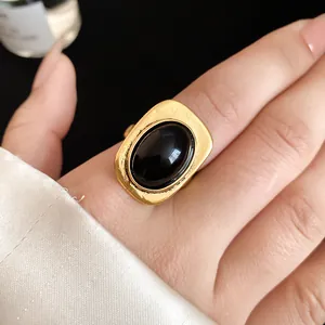 Close-up detail of a vintage gold rectangular ring featuring a large oval black stone on a finger