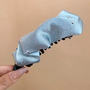 Dettaglio della clip a banana in raso plissettato azzurro con accenti di strass