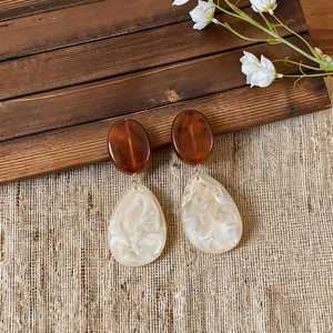 Macro detail of retro resin teardrop earrings with amber oval and marbled cream drop