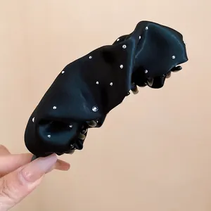Primo piano di un fermaglio a banana in tessuto plissettato nero con accenti di strass