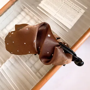 Dettaglio di un fermaglio a banana in raso plissettato marrone con strass scintillanti