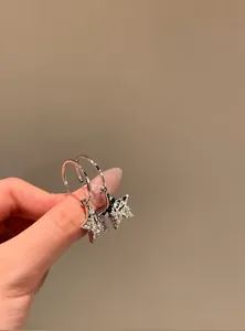 Close-up of silver Y2K star hoop earrings with sparkling stones held by hand.