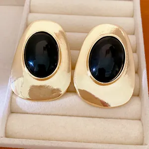 Macro detail of elegant gold-tone stud earrings with oval black stones in jewelry box