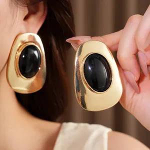 Close-up of chunky gold earrings with black oval stones showing texture and size