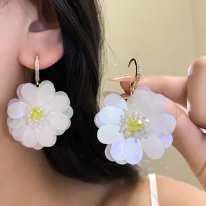 Close-up of white iridescent fabric flower earrings with sparkling crystal-set gold hooks