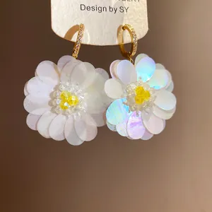Close-up detail of white iridescent fabric flower earrings with yellow beads