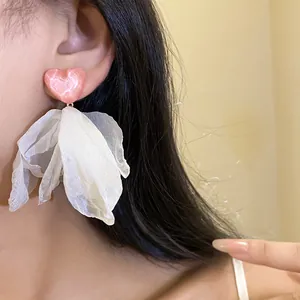 Detail of pink glitter heart stud earrings featuring white organza petal tassels on a model.