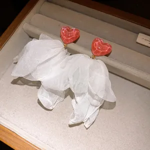 Detail view of elegant white fabric flower tassel earrings with red heart studs.