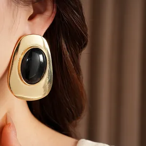 Close-up of elegant gold oval earrings with black cabochon stone on model