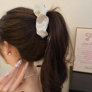 Dettaglio di un fermaglio per capelli a banana in tessuto a pieghe crema con strass