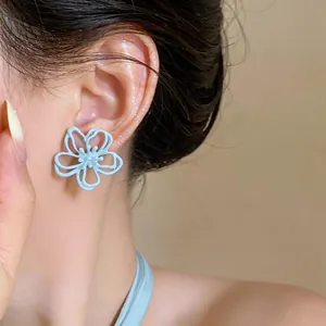 Nahaufnahme eines eleganten himmelblauen hohlen Blumenohrsteckers, der am Ohr getragen wird