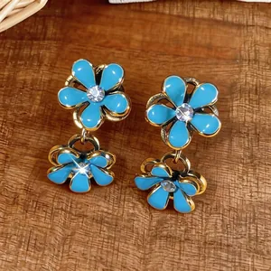 Elegant enamel blue flower drop earrings with sparkling rhinestones on wood background