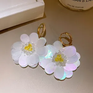 Close-up of elegant white fabric flower earrings with sparkling gold hooks.