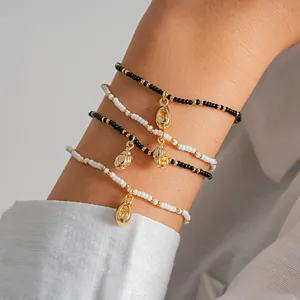 Detail view of beaded bracelets with gold conch and shell charms on model's wrist