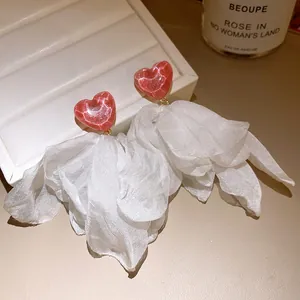 Close-up of elegant pink glitter heart earrings with large white fabric floral tassels