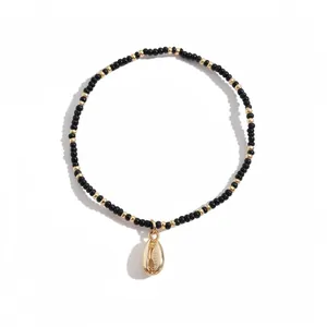 Minimalist black and gold seed bead stretch bracelet with a golden cowrie shell